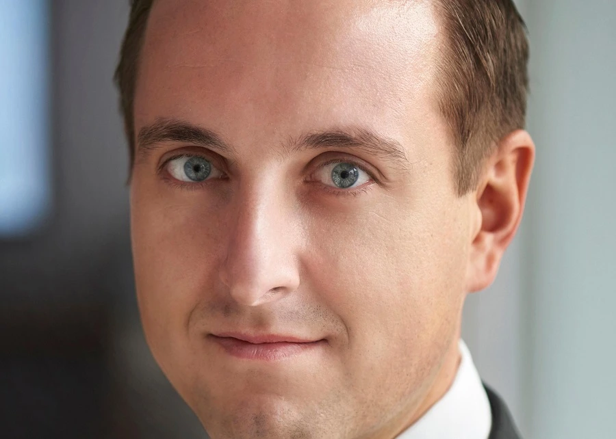 middle aged man in black blazer smiling against grey background